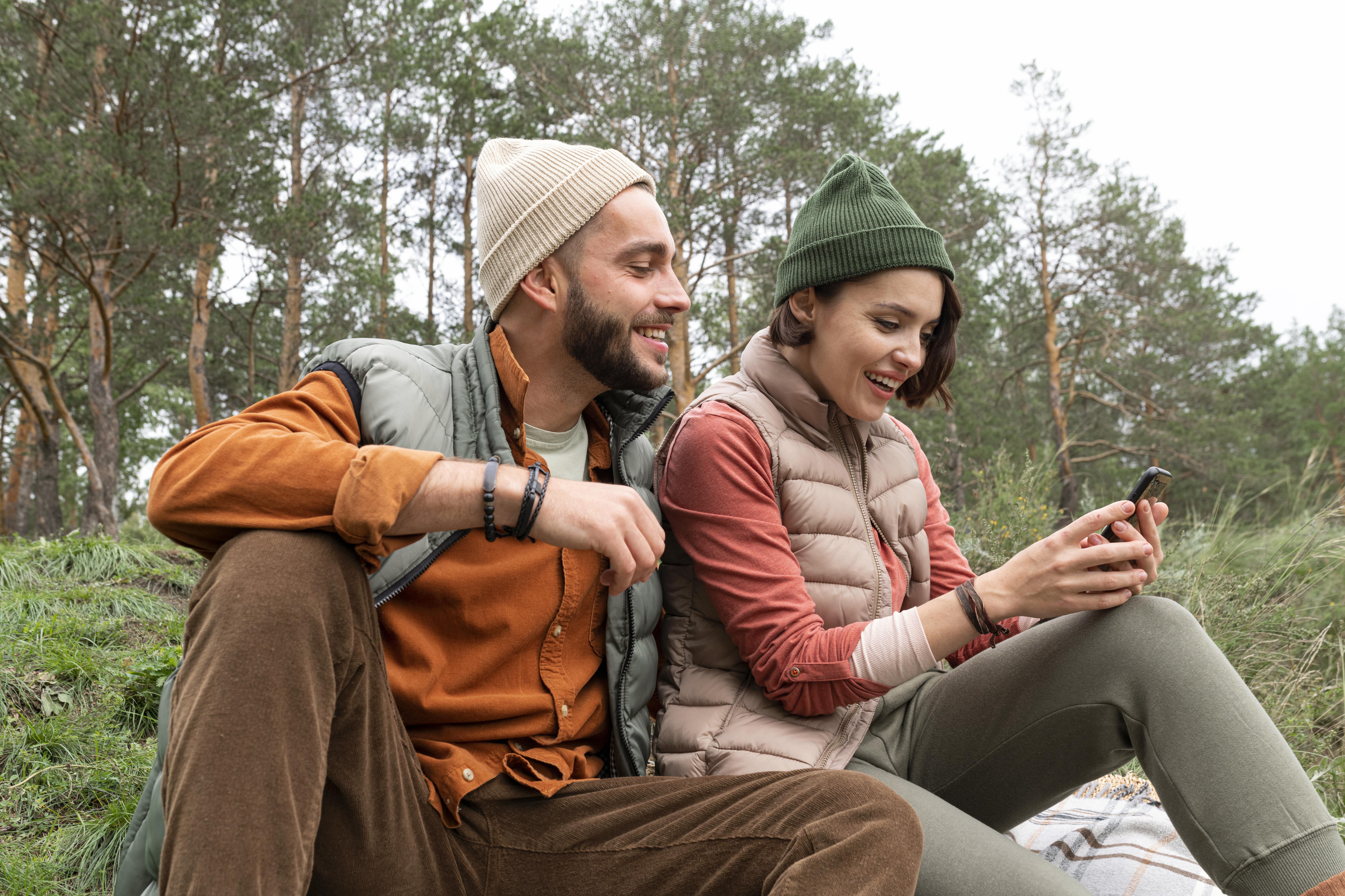 mid-shot-happy-couple-sitting-grass-looking-phone