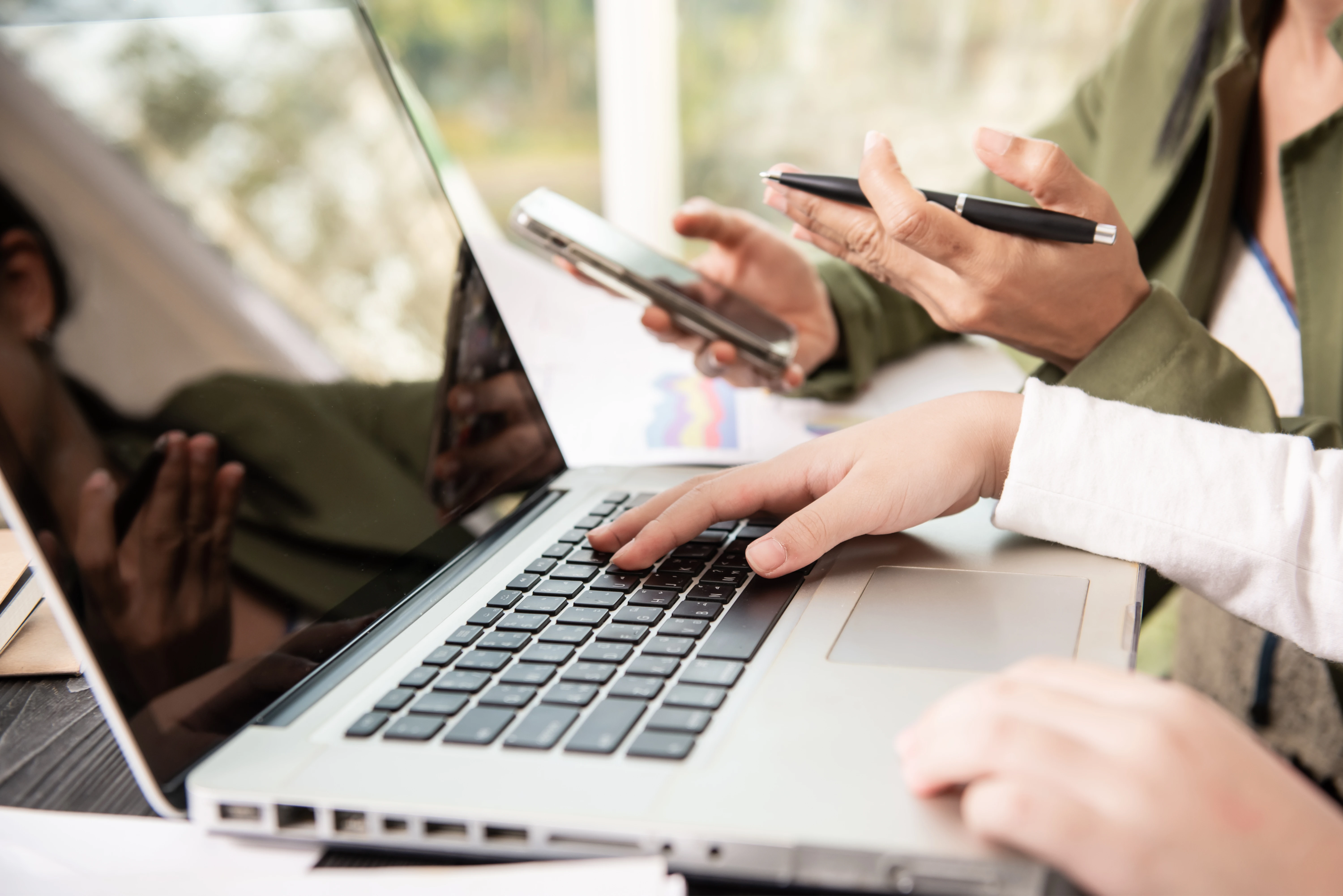 side_view_businesswoman_s_hands_using_laptop_computer_placed_messy_office_desktop_teamwork_with_business_people_analysis_cost_graph_desk_meeting_room_1